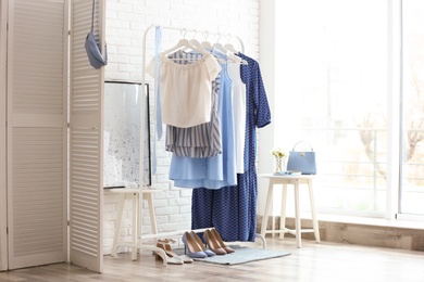 Photo of Wardrobe rack with women's clothes and different shoes at white brick wall in room