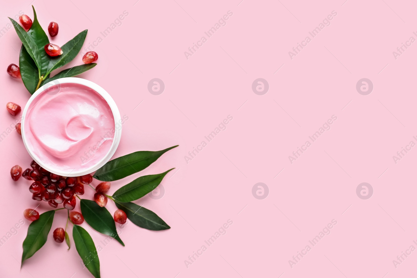 Photo of Fresh pomegranate and jar of facial mask on pink background, flat lay. Space for text