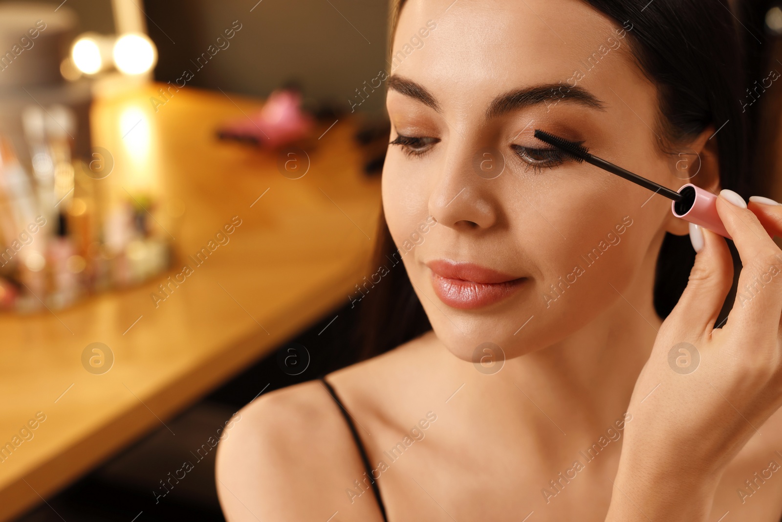 Photo of Beautiful young woman applying mascara in dressing room, closeup. Space for text