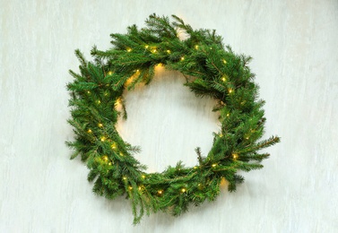 Photo of Beautiful Christmas wreath with festive lights on white wooden background, top view