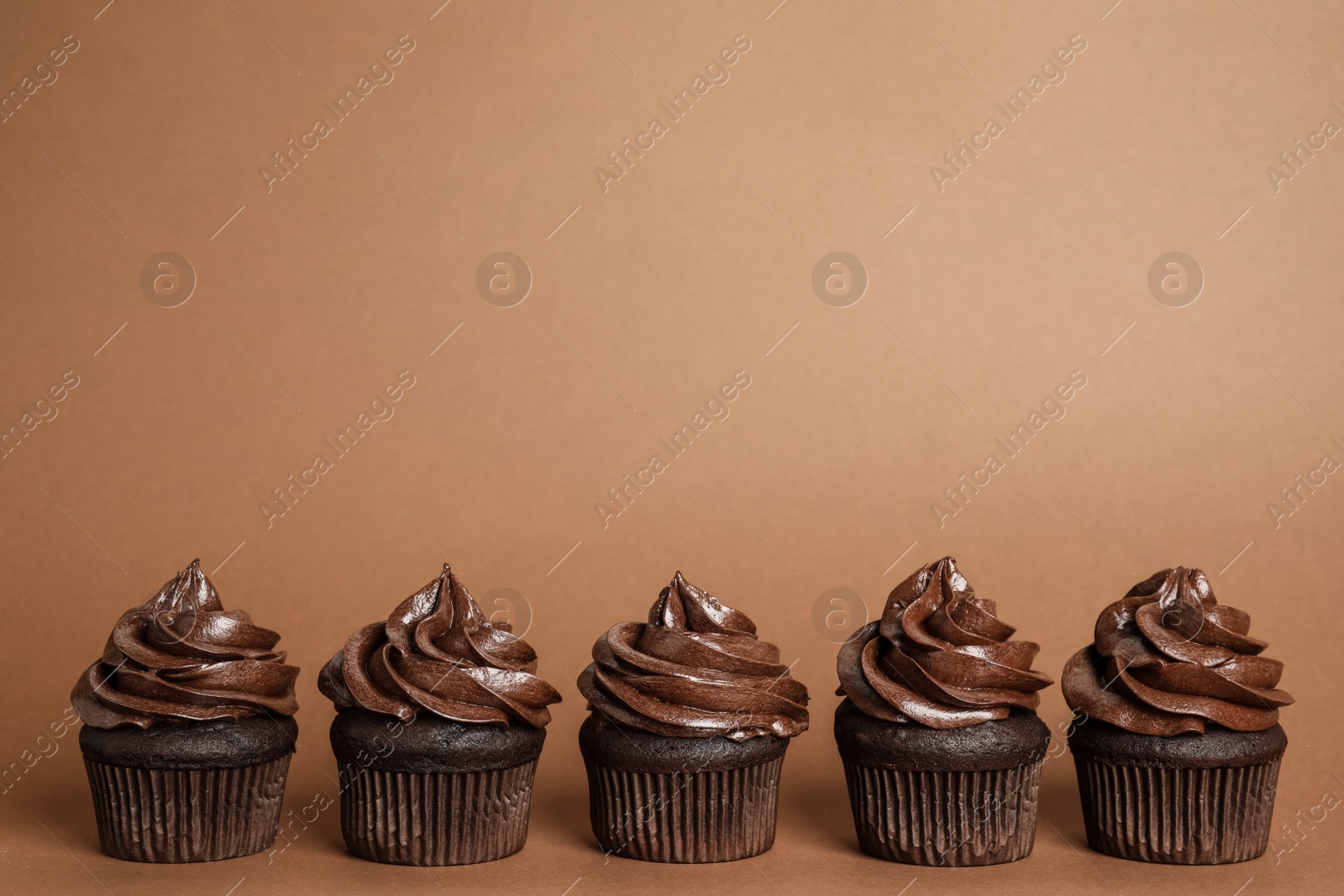Photo of Delicious chocolate cupcakes with cream on brown background. Space for text
