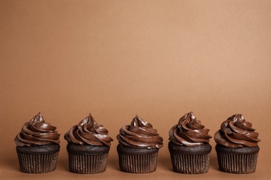 Delicious chocolate cupcakes with cream on brown background. Space for text