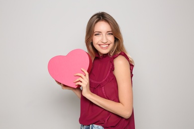 Portrait of beautiful smiling girl with heart shaped gift box on light background. International Women's Day