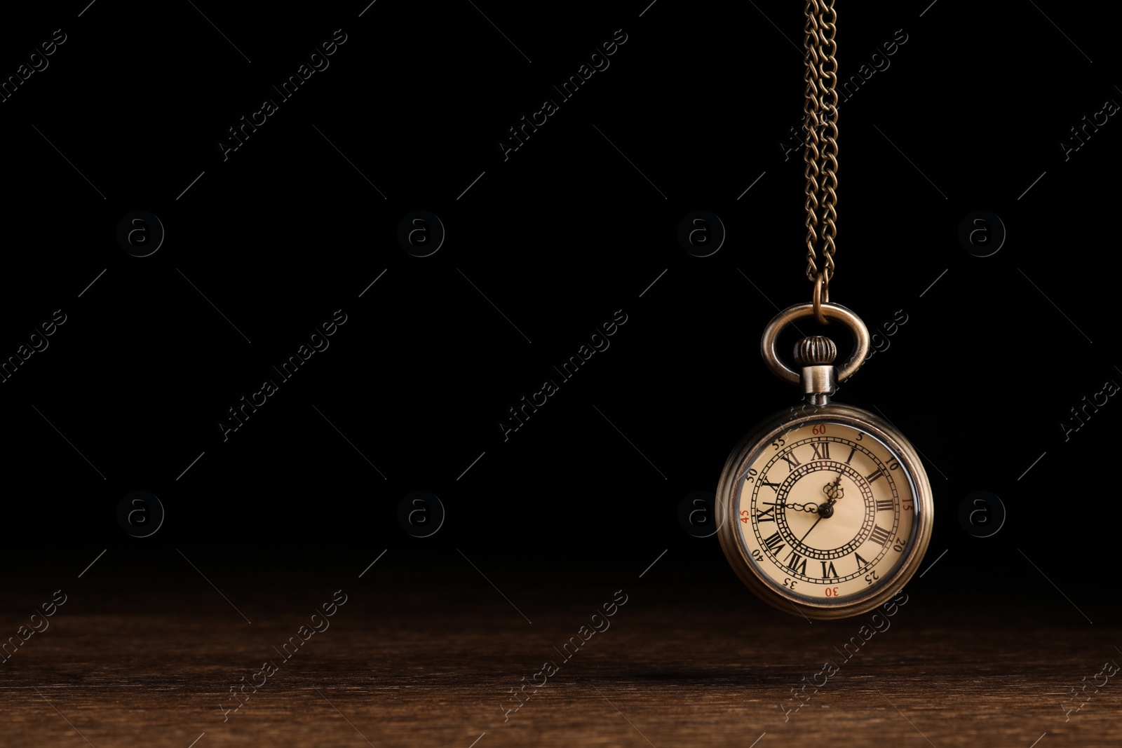 Photo of Stylish pendulum above wooden table on black background, space for text. Hypnotherapy session