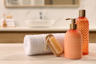 Photo of Liquid soap in glass dispenser, bottle of shower gel brush and towel on white wooden table indoors