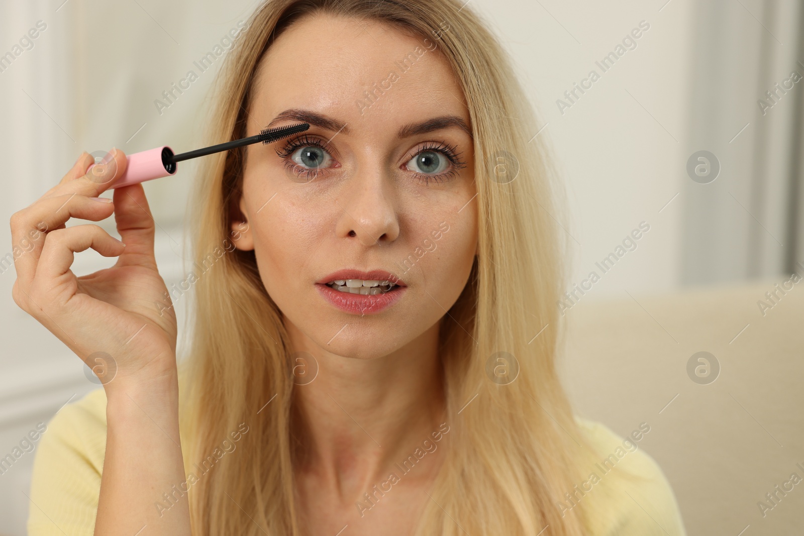 Photo of Beautiful woman applying mascara with brush indoors, closeup