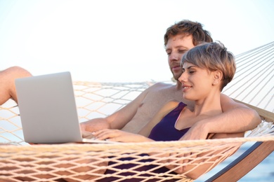 Young couple resting with laptop in hammock on beach