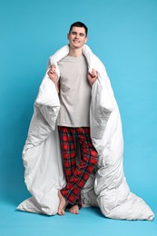 Happy man in pyjama wrapped in blanket on light blue background