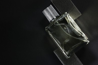 Stylish presentation of luxury men`s perfume in bottle on black background, top view. Space for text