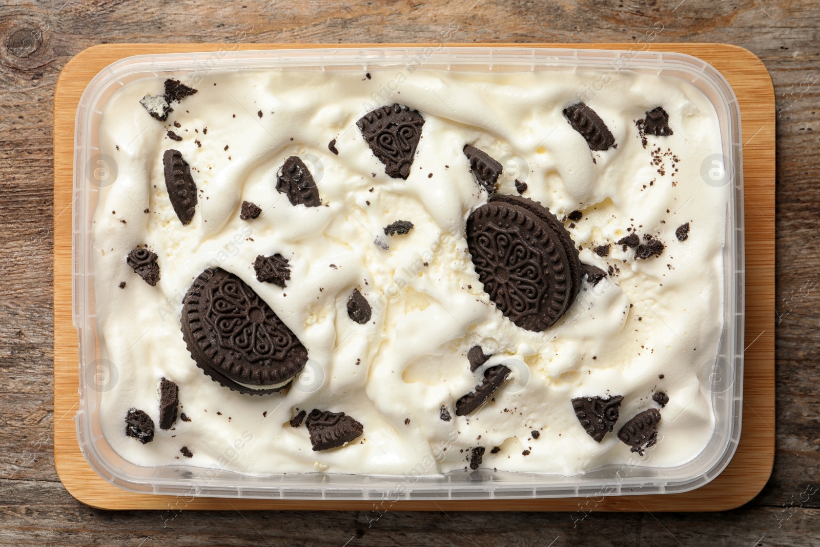 Photo of Container of ice cream with chocolate sandwich cookies on wooden background, top view