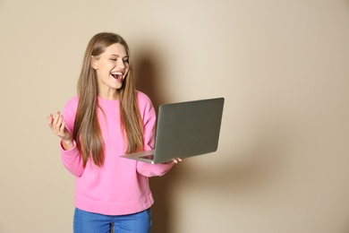 Photo of Emotional young woman with laptop celebrating victory on color background. Space for text