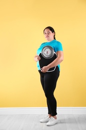 Overweight woman in sportswear with scales near color wall