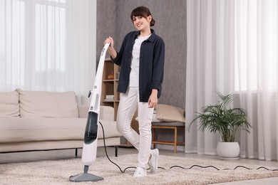 Photo of Happy young housewife vacuuming carpet at home