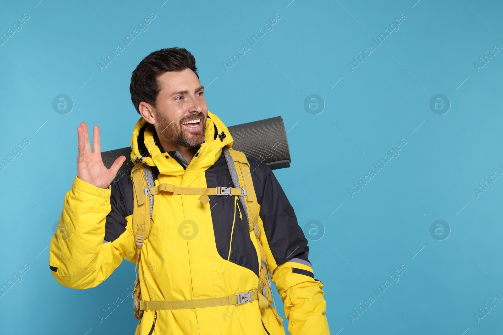 Photo of Happy tourist with backpack on light blue background, space for text