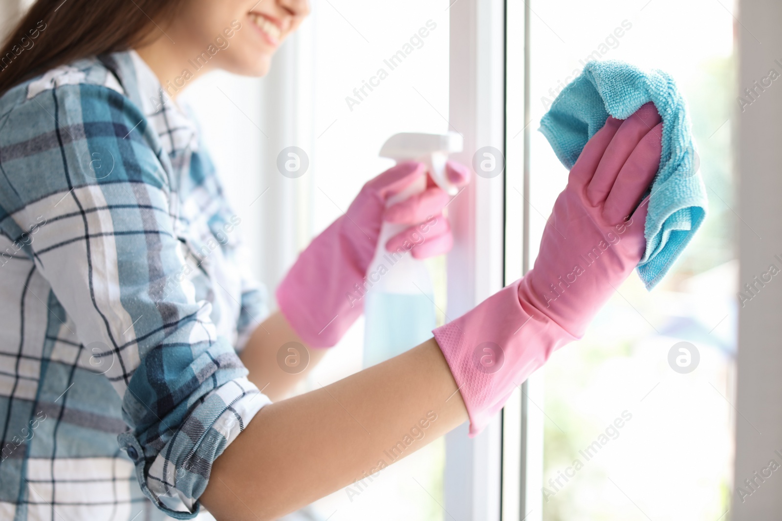 Photo of Young woman cleaning window glass at home