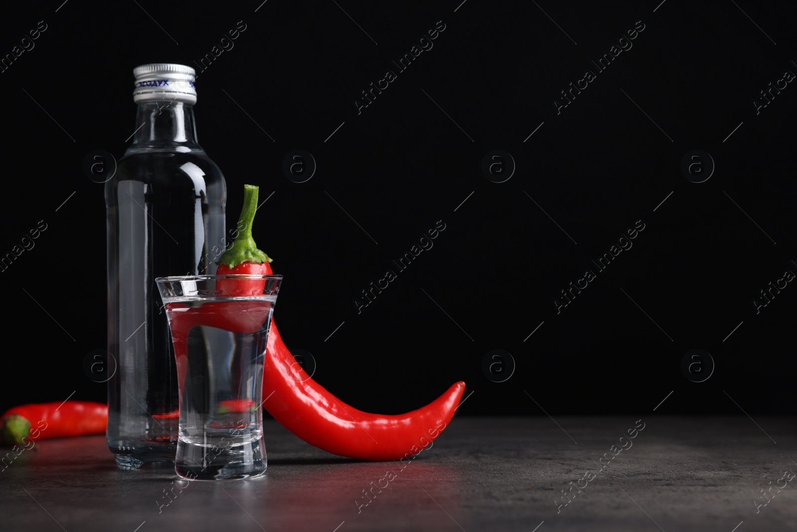 Photo of Red hot chili peppers and vodka on grey table against black background, space for text