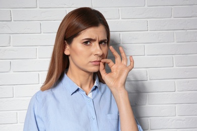 Photo of Woman zipping her mouth near brick wall, space for text. Using sign language