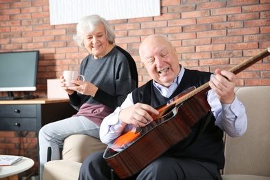 Elderly man playing guitar for his wife on sofa in living room