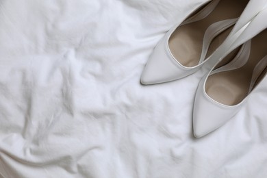 Photo of Pair of wedding high heel shoes on white fabric, flat lay. Space for text