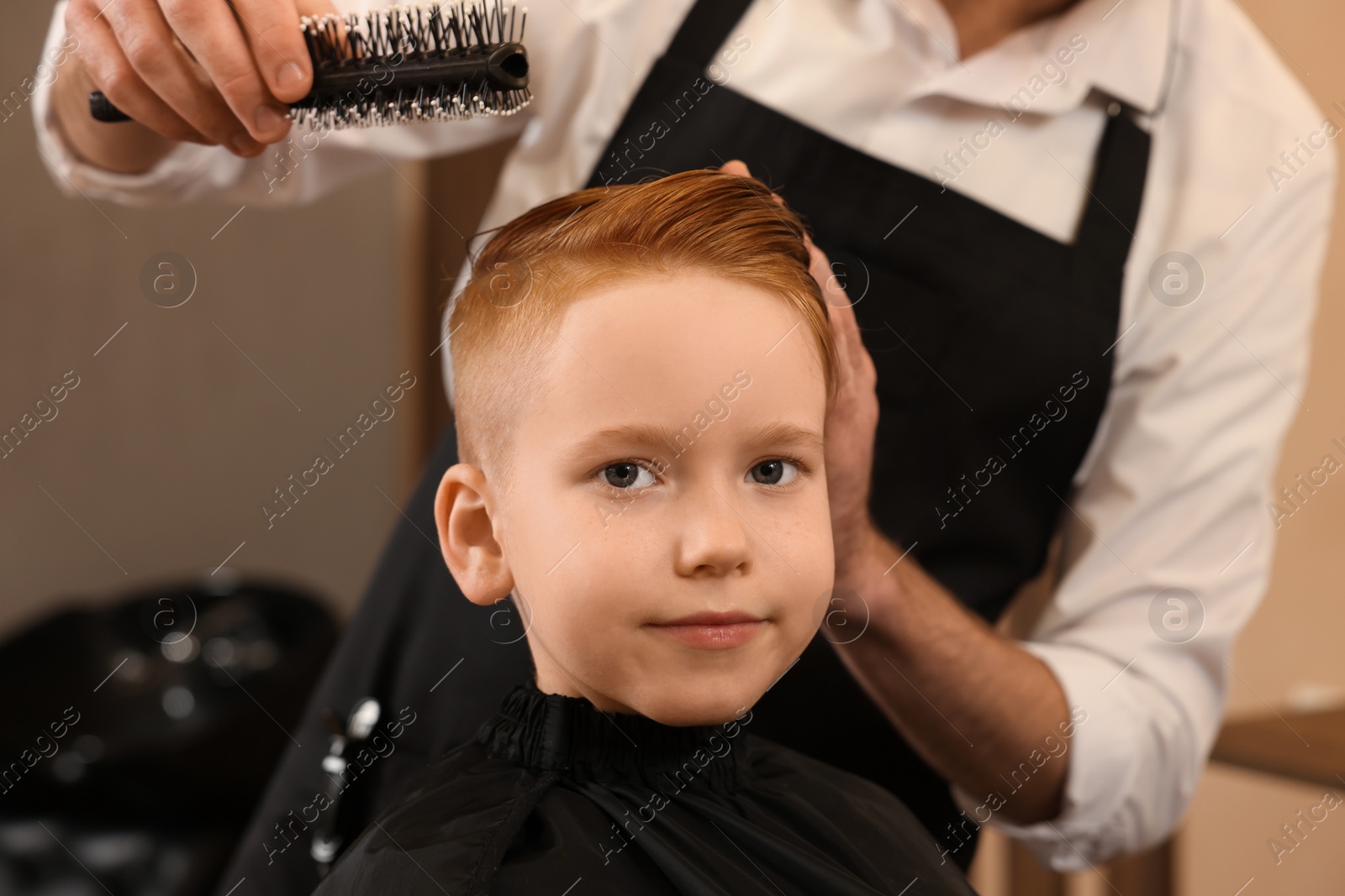 Photo of Professional hairdresser working with boy in beauty salon, closeup