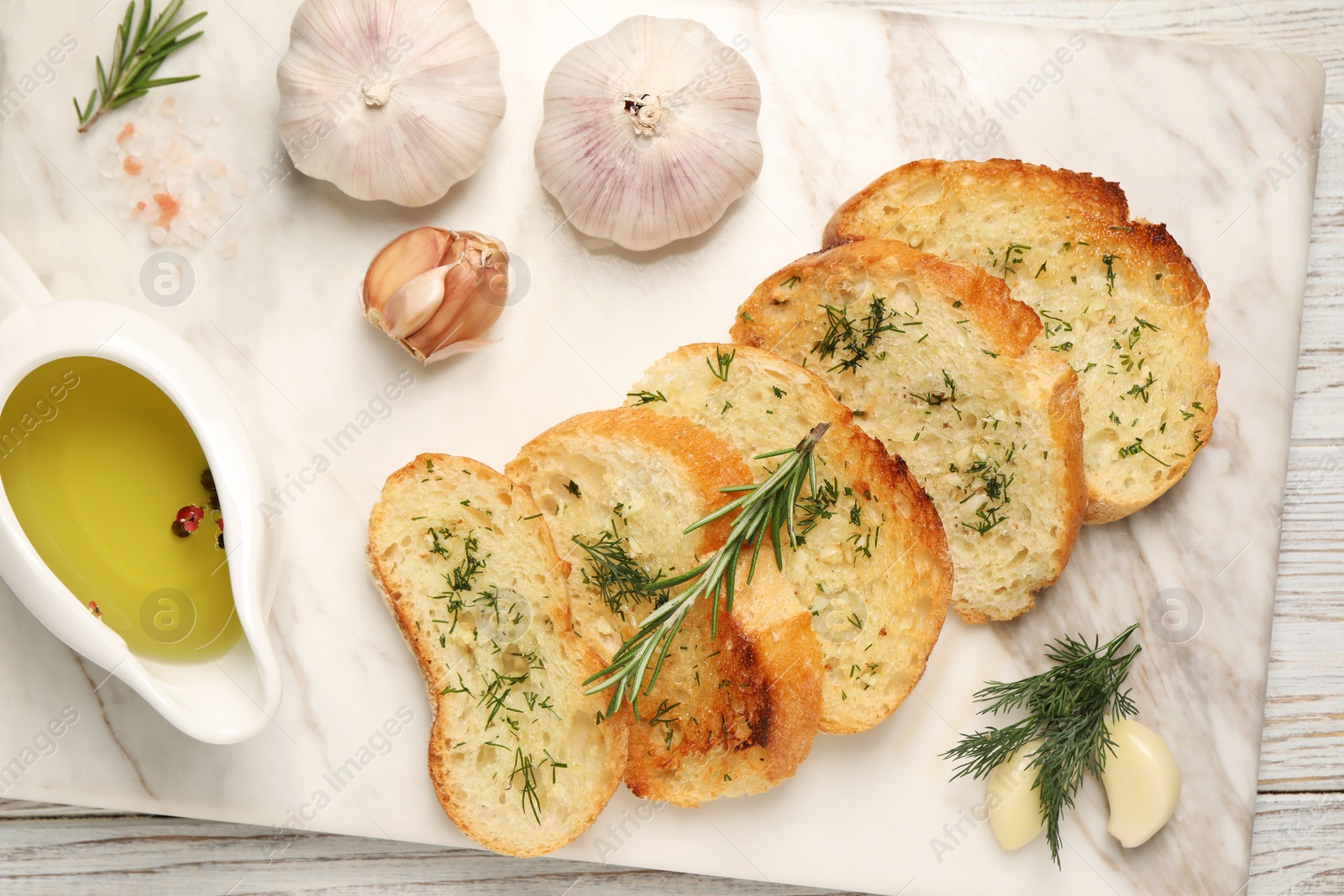 Photo of Tasty baguette with garlic, dill, rosemary and oil on white wooden table, top view