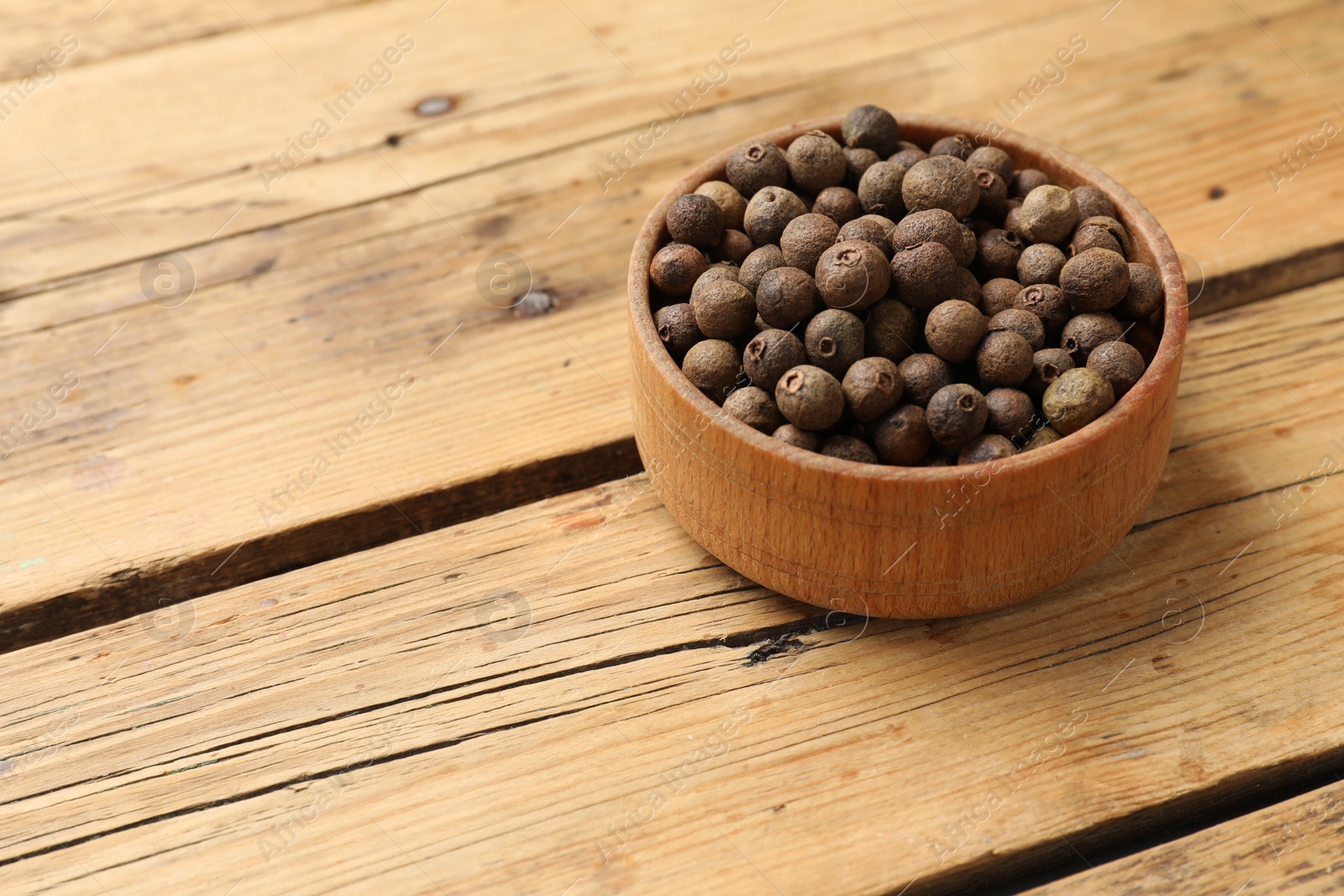 Photo of Dry allspice berries (Jamaica pepper)in bowl on wooden table, space for text