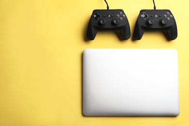 Photo of Video game controllers and laptop on color background, top view with space for text