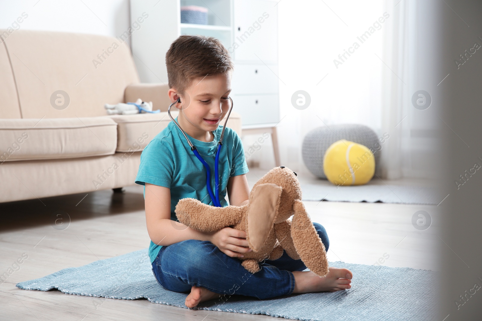 Photo of Cute child imagining himself as doctor while playing with stethoscope and toy bunny at home
