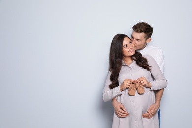 Photo of Pregnant woman and her husband holding little shoes on color background. Space for text