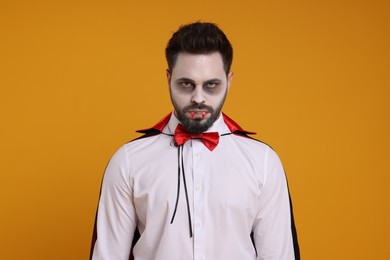 Man in scary vampire costume with fangs on orange background. Halloween celebration