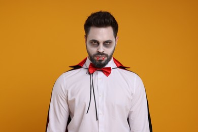 Photo of Man in scary vampire costume with fangs on orange background. Halloween celebration