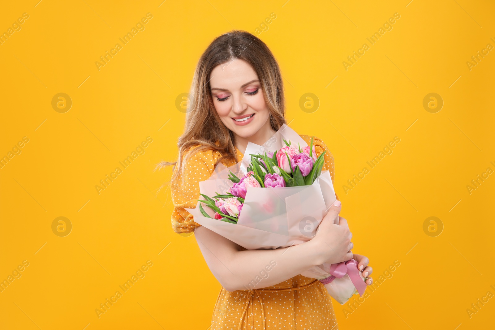 Photo of Happy young woman with bouquet of beautiful tulips on yellow background