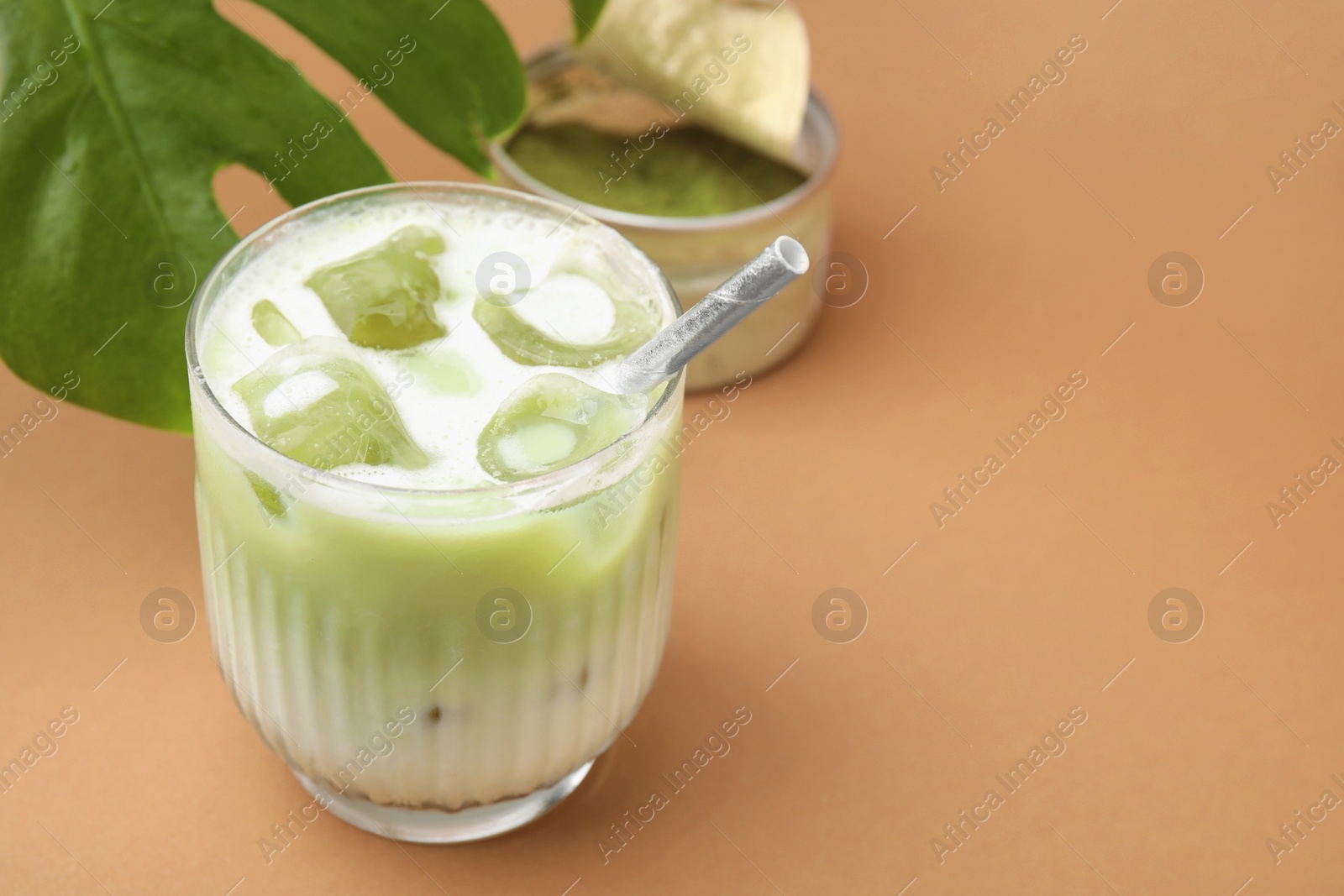 Photo of Glass of tasty iced matcha latte and leaf on light brown background. Space for text