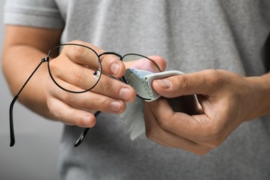 Photo of Man wiping glasses with microfiber cloth on light grey background, selective focus