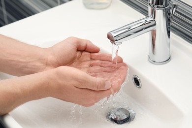 Photo of Man using water tap to wash hands in bathroom, closeup