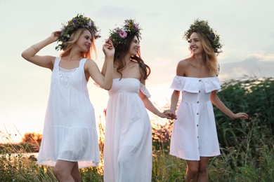 Young women wearing wreaths made of beautiful flowers outdoors at sunset
