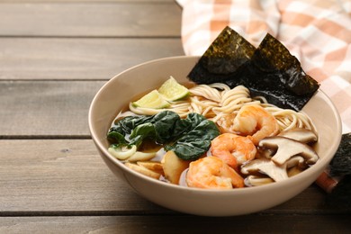 Photo of Delicious ramen with shrimps and mushrooms in bowl on wooden table, closeup with space for text. Noodle soup