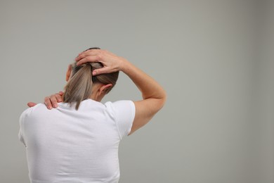 Mature woman suffering from pain in her neck on grey background, back view. Space for text