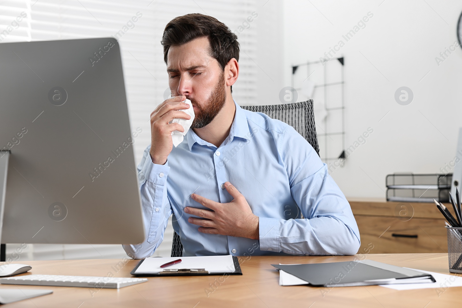 Photo of Sick man with tissue coughing at workplace in office