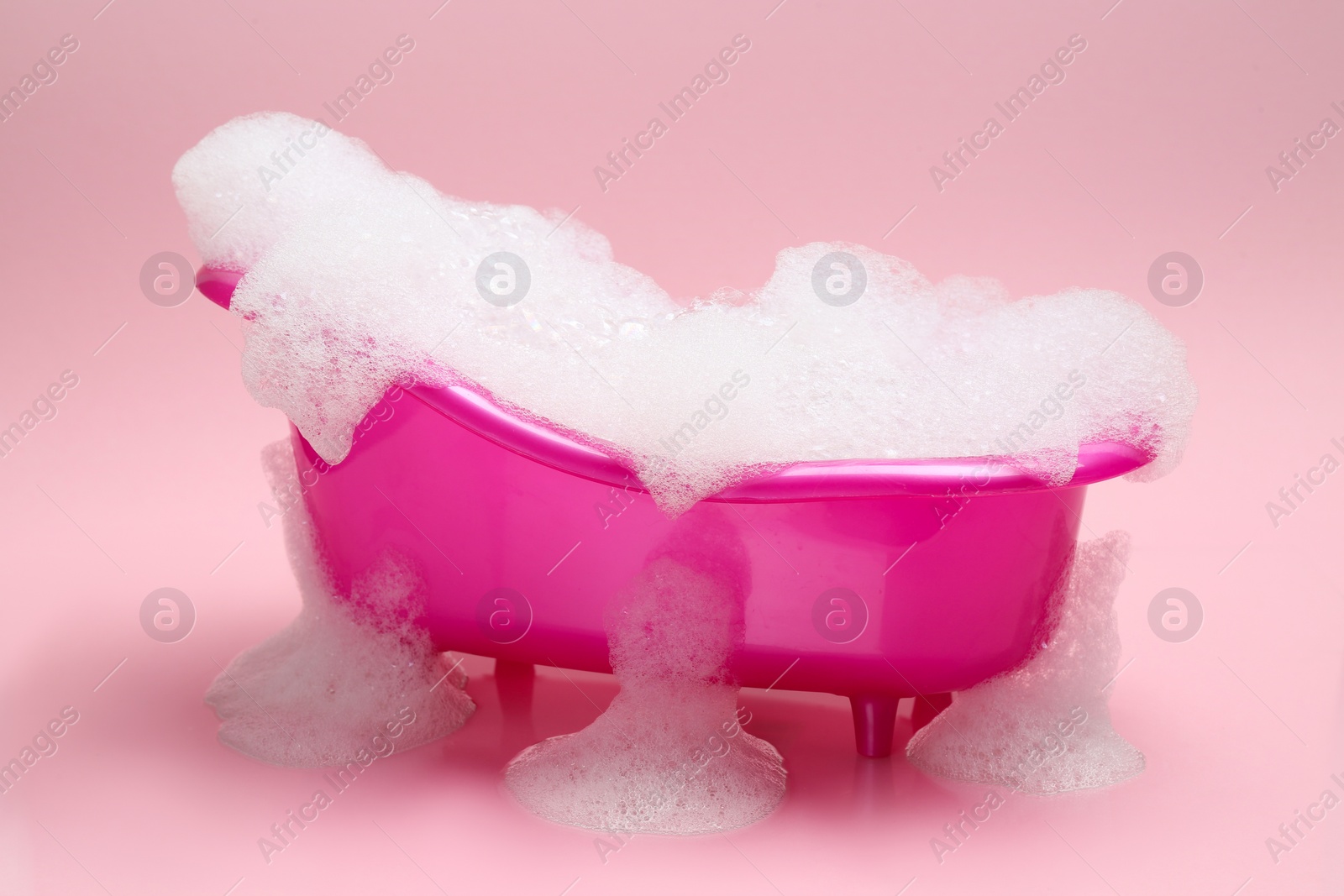 Photo of Toy bathtub overflowing with foam on pink background