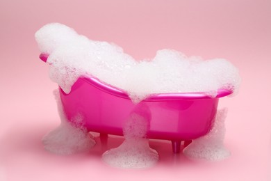 Photo of Toy bathtub overflowing with foam on pink background