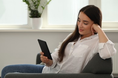 Photo of Young woman using e-book reader at home