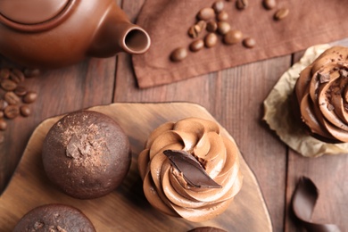 Delicious chocolate muffins and cupcakes decorated with cream on wooden table, flat lay