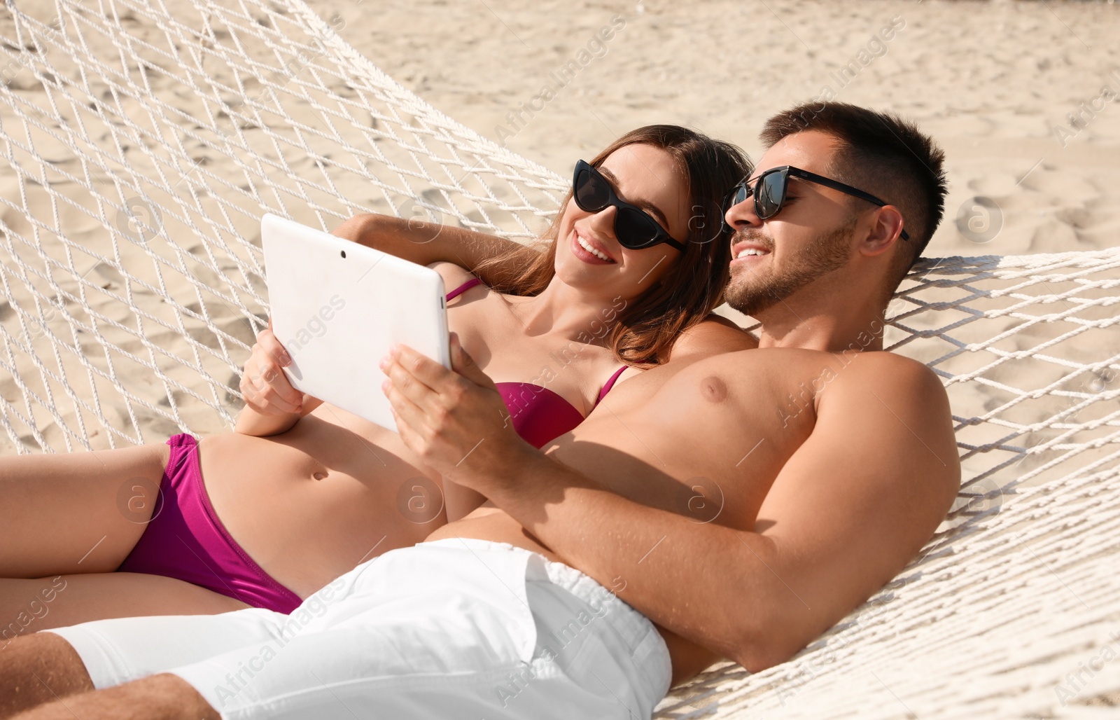 Photo of Young couple with tablet relaxing in hammock on beach