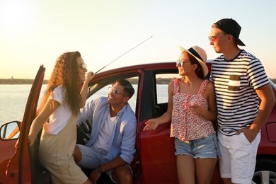Photo of Happy friends near car outdoors at sunset. Summer trip