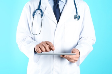 Male doctor holding modern tablet on color background, closeup