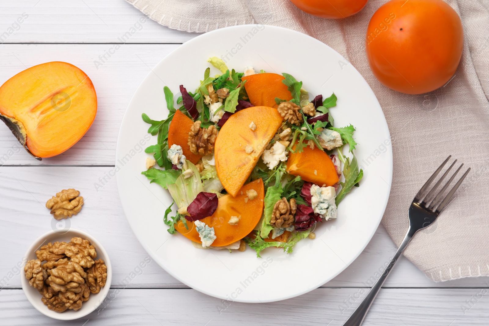 Photo of Delicious persimmon salad and fork on white wooden table, flat lay