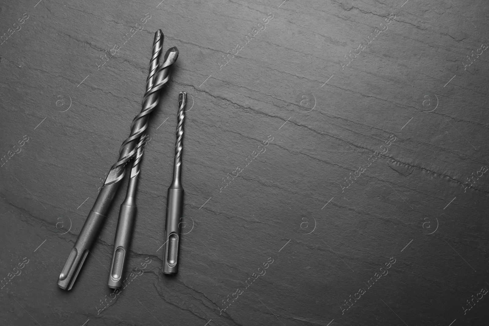 Photo of Different drill bits on black table, flat lay. Space for text