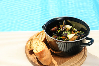 Photo of Mussels with lemon slices in pot near swimming pool