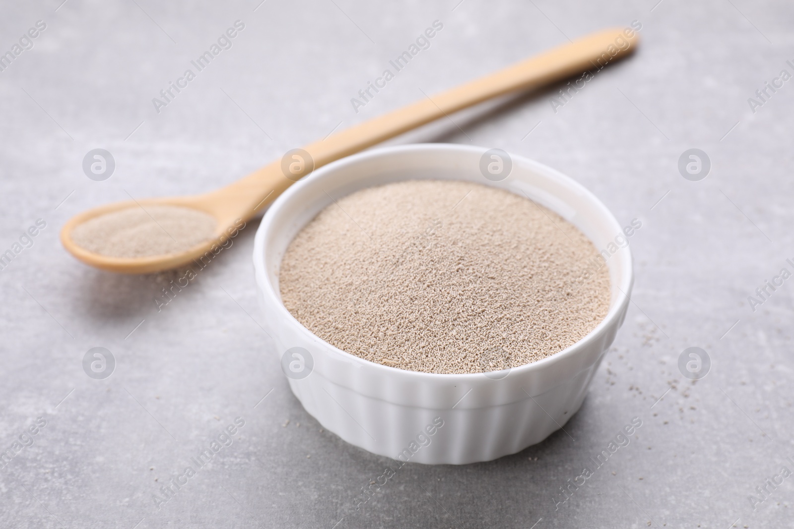 Photo of Bowl and spoon with active dry yeast on light grey table, closeup